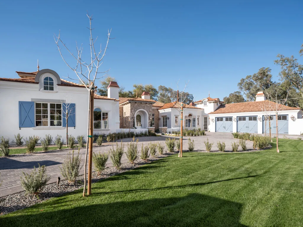 Completed Spanish Mission-style luxury residence with white stucco, clay tile roofs, blue shutters and a circular brick driveway